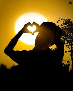 the silhouette of a person making a heart shape with their hands in front of the sun