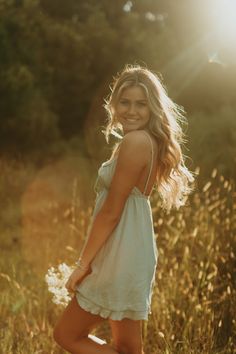 a beautiful young woman posing for a photo in tall grass with the sun shining behind her