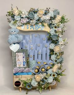 a blue teddy bear sitting on top of a wooden bench surrounded by flowers and other items