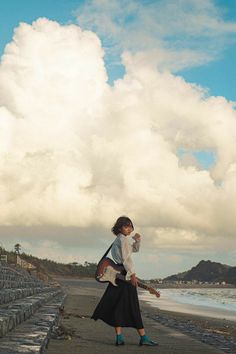 a woman is walking on the beach with an umbrella in her hand and clouds in the background