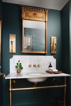 a white sink sitting under a bathroom mirror next to a gold faucet mounted on a wall