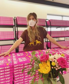 a woman wearing a face mask standing in front of pink boxes with yellow and white flowers