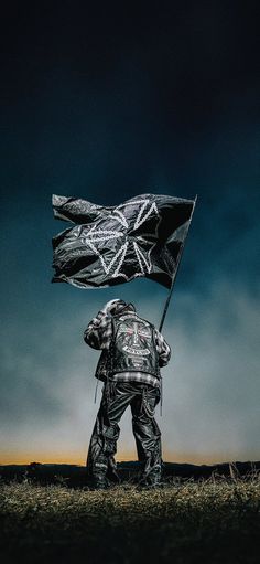 a man standing in the grass holding a black and white flag under a dark sky