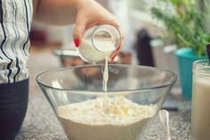 a person pouring milk into a glass bowl