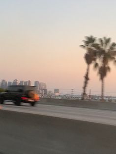 a black truck driving down the road next to palm trees