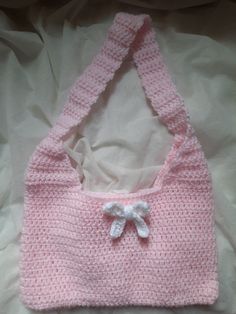 a pink crocheted purse with a bow on the front and side, laying on a bed