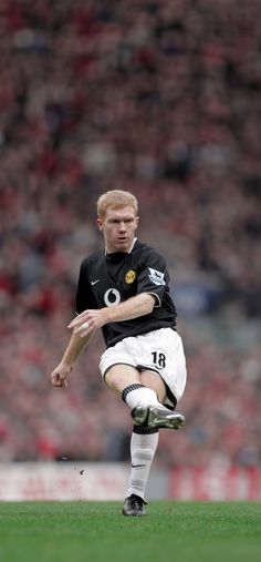 a young man kicking a soccer ball on top of a field with people in the background