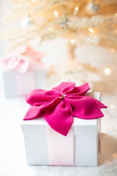 two white gift boxes with pink bows on them sitting in front of a christmas tree