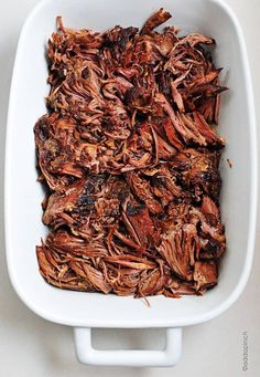 a square white dish filled with meat on top of a table