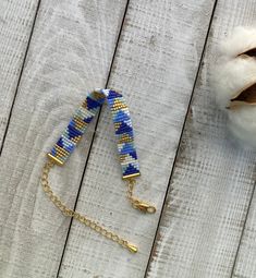 a blue and white beaded bracelet sitting on top of a wooden table next to a cotton ball