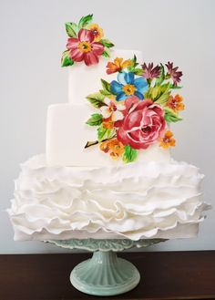 a three tiered cake with flowers painted on it's side and ruffles around the edges