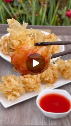 a person holding chopsticks with food on them and dipping sauce in the bowl