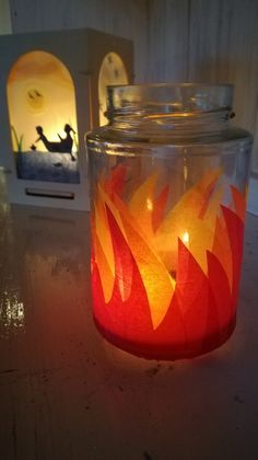 a lit candle sitting on top of a table next to a glass jar filled with fire