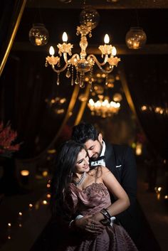 a man in a tuxedo and woman in a dress hugging under a chandelier