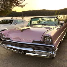 two old cars parked next to each other in a parking lot near the water at sunset