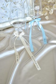 two empty wine glasses sitting on top of a white cloth covered tablecloth with blue ribbon