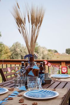 an outdoor table set with plates, glasses and bottles filled with cookies on it in front of a wooden fence