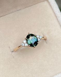 a ring with an oval shaped green stone surrounded by small white diamonds in a box