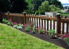 a wooden fence with flowers growing on the side and grass in the front yard behind it