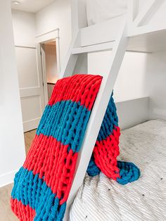 a red and blue knitted pillow sitting on top of a white bunk bed next to a ladder