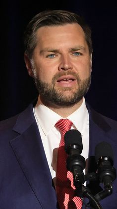 a man in a suit and tie speaking into microphones