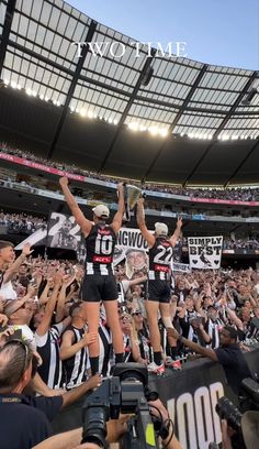 two women standing on top of each other in front of a crowd holding up signs