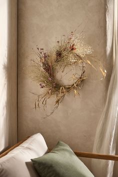 a dried wreath hangs on the wall above a bed with white sheets and green pillows