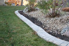 a garden bed with rocks and plants in the grass next to a brick walkway that leads to a house