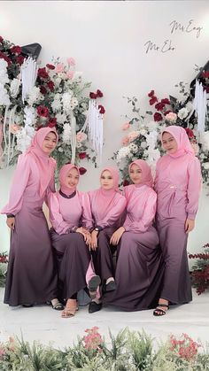 the women are posing for a photo in front of flowers and greenery with their headscarves pulled back