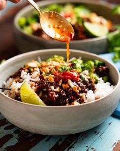 someone is pouring sauce into a bowl filled with rice, vegetables and other things in it