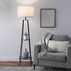 a living room with a gray couch and white brick wall behind the chair is a lamp that has a plant on it