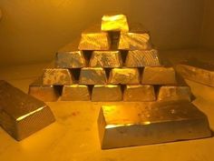 a pile of gold bars sitting on top of a table next to a lit lamp