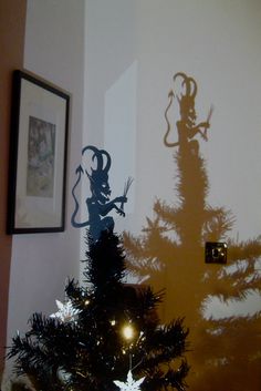 a christmas tree with the shadow of a cat on it's side and an image of a demon on the wall behind it