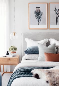 a bed with pillows and blankets on top of it, next to two framed pictures