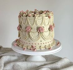 a white cake with pink flowers on it sitting on top of a table next to a gray cloth