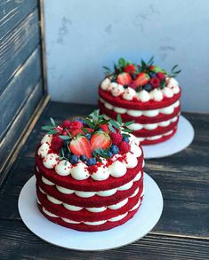 two red velvet cakes with white frosting and strawberries on top, sitting on plates