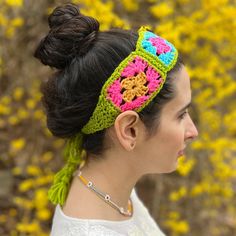 a woman wearing a crocheted headband in front of yellow and pink flowers