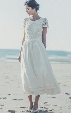 a woman standing on top of a sandy beach next to the ocean wearing a white dress