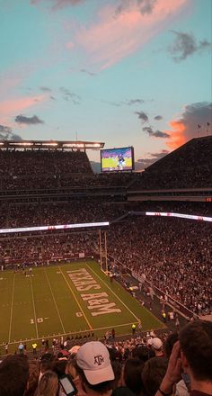 a football stadium filled with lots of people watching the sun go down on an empty field