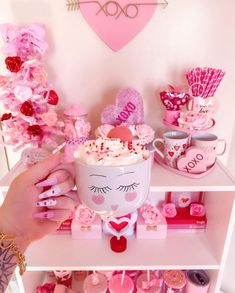 a person holding a cup in front of a shelf filled with valentine's day decorations