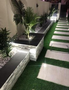 an outdoor area with artificial grass and plants on the side of the building at night