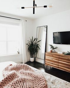 a bedroom with a bed, dresser and large mirror in the corner that has a plant on it