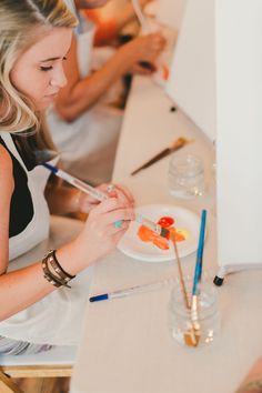 a woman sitting at a table with paintbrushes in front of her