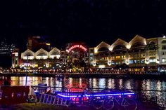 a bike parked on the side of a river next to tall buildings at night time