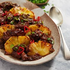 a plate filled with pineapples and meat on top of a table next to a spoon