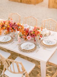 the table is set with white plates and gold place settings, along with colorful flowers