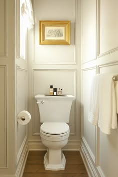 a white toilet sitting in a bathroom next to a wall mounted painting on the wall