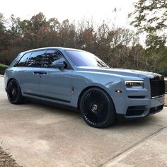 a grey rolls royce parked in front of some trees