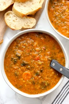 two bowls filled with soup next to slices of bread on top of a white table