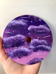 a hand holding up a purple disc with stars and clouds on it